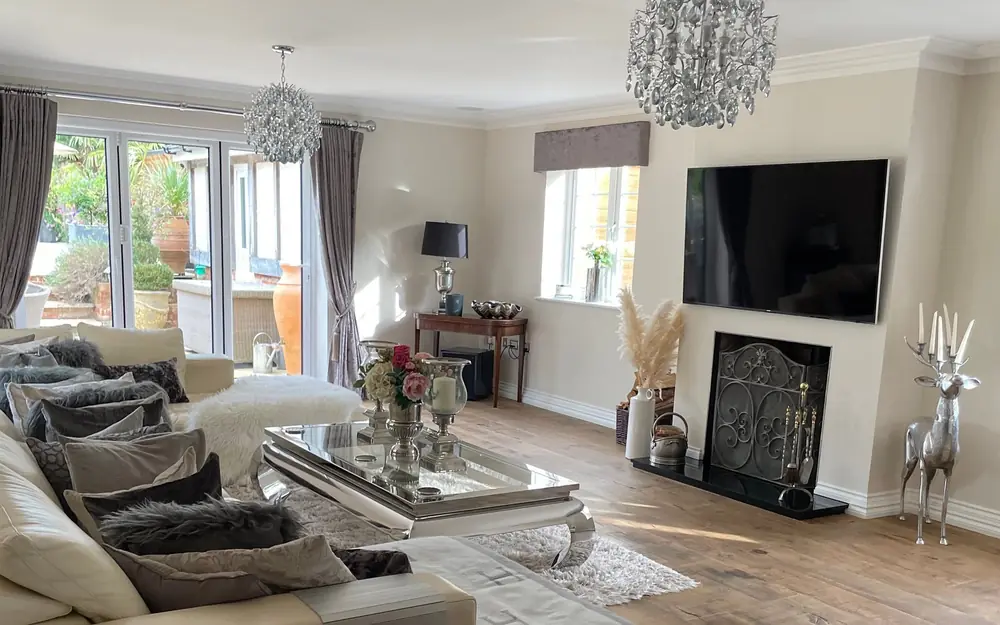 Finished living room with a television above the fireplace and two pendant chandeliers